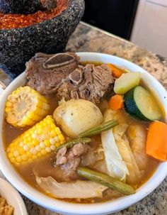 a bowl of soup with meat, vegetables and corn on the cob