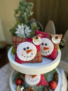 two snowmen sitting on top of a cake plate with christmas decorations in the background