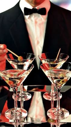 a man in a tuxedo is holding three martini glasses on a serving tray