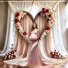 a pregnant woman standing in front of a heart shaped backdrop with roses and greenery