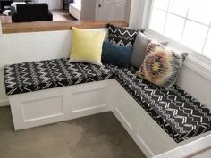 a corner bench with pillows on it in the middle of a room next to stairs