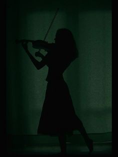 a woman playing violin in the dark with her arms behind her back and head turned