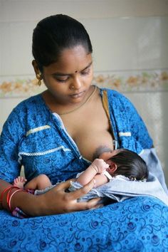 a woman holding a baby in her arms while sitting on top of a bed next to a wall