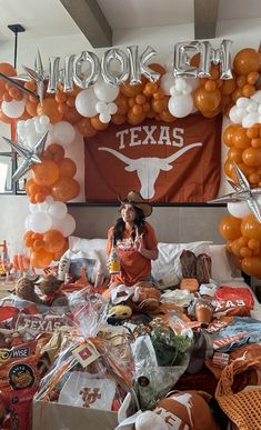 a woman sitting on top of a bed surrounded by orange and white balloons in the shape of texas