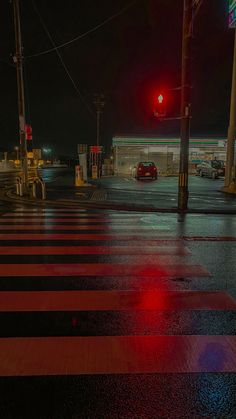 a red traffic light sitting above a cross walk at an intersection on a rainy night