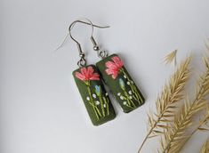 the earrings are decorated with pink flowers on green fabric and silver earwires hanging from hooks