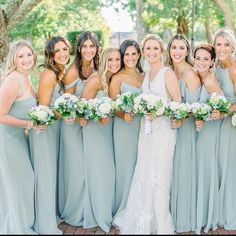 a group of women standing next to each other in front of trees and bushes with bouquets