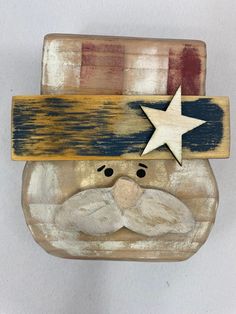 a wooden santa clause with a star on his head and beard is hanging from a wall