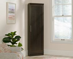 a tall wooden cabinet sitting in the corner of a room next to a chair and potted plant