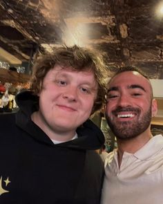 two men are posing for the camera in a restaurant with one man wearing a black hoodie