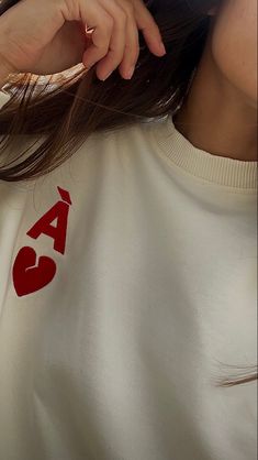 a woman wearing a white sweatshirt with red letters on the front and back, she is holding her hair up to her face