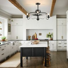 a large kitchen with white cabinets and black island in the center is lit by an antique chandelier