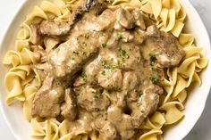 a white bowl filled with pasta and meat covered in gravy