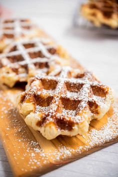 two waffles on a cutting board covered in powdered sugar and sitting next to each other