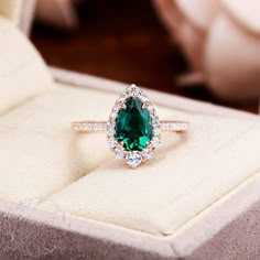 a ring with a green stone surrounded by white diamonds in a box on top of a table