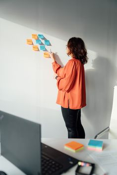 a woman standing in front of a white wall with sticky notes on it and looking at a laptop