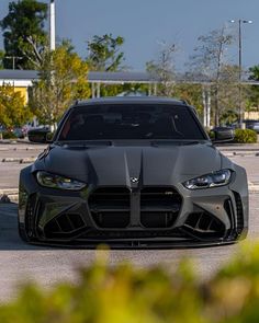 the front end of a black sports car parked in a parking lot with other cars behind it