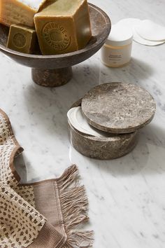 some soaps and other items on a marble counter top, including a bowl with two pieces of soap