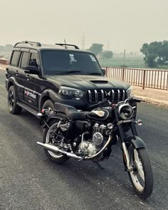 a black jeep is parked next to a black motorcycle on the road in front of a truck