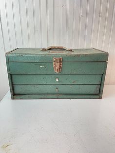 an old green metal tool box sitting on top of a white counter next to a wall