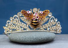 This beautiful honey bee crown features all glass rhinestones and is truly stunning.  The enamel, metal bee features purple rhinestones on the wings.  The circumference of the tiara is about 13 inches.   At the highest point on the front, it is 2 inches tall.  There are two loops at the base for attachment.  Fits adults and children 5 and up.   Ships in a gift box for easy gift giving! Shipping Details: All items will be shipped First Class by the United States Postal Service. An option to upgrade shipping to Priority or Express Service is available upon checkout for USA orders. You will be provided with a tracking number once your order has been shipped via email. Current processing times are shown in each listing. Shipping within the US typically (but not always), takes 3-6 business days Bride To Bee, Bee Crown, Tiara Flower, Bee Hat, Metal Bee, Bee Wings, Flower Girl Headband, Crown Gold, Bee Dress