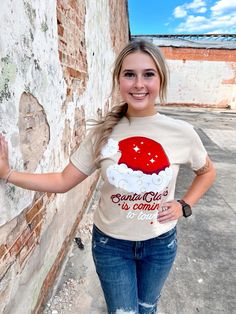 a woman standing next to a brick wall wearing a santa clause t - shirt and ripped jeans