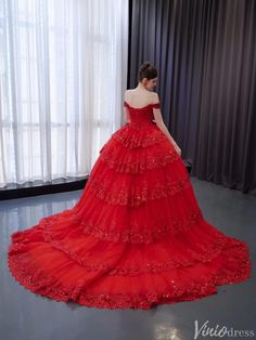 a woman in a red wedding dress looking down at the floor with curtains behind her