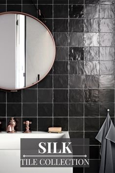 a bathroom with black tiles and a round mirror above the sink is featured in this article