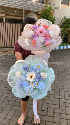 a woman holding two large bouquets of flowers on top of each other in front of a building