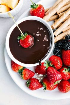 a plate with strawberries, crackers and chocolate dip on it next to fruit