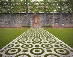 an outdoor garden with grass and stone walls, surrounded by trees and bushes is shown in front of a wooden door