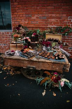 a wooden table topped with lots of different types of flowers next to a brick wall