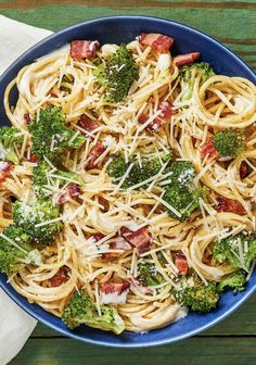 a blue bowl filled with pasta and broccoli on top of a wooden table