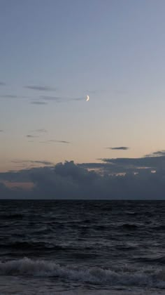 the moon is setting over the ocean with waves