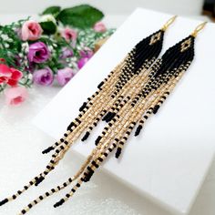 a pair of black and gold beaded earrings sitting on top of a white box