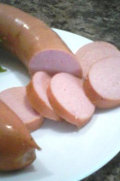 a white plate topped with slices of sausage next to a pickle on a green leaf