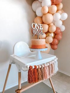 a cake sitting on top of a wooden table next to a balloon wall and chair