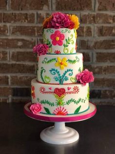 a multi - tiered cake decorated with flowers on a table next to a brick wall