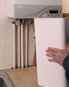 a person is holding up a white box in front of a kitchen sink with a water dispenser on the wall