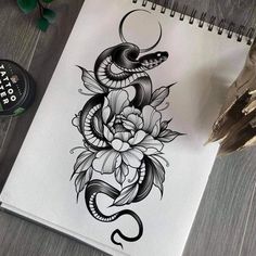 a spiral notebook with a snake and flowers on the cover, next to a pen