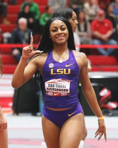 a woman in a purple bathing suit pointing to the side while standing on a track