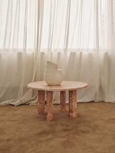 a table with a vase sitting on top of it in front of a curtained window