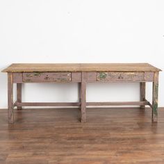 an old wooden table sitting on top of a hard wood floor next to a white wall