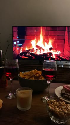 a table topped with glasses of wine and food next to a fire in the fireplace