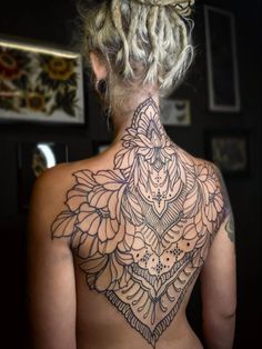 the back of a woman's neck with an intricate tattoo design on her chest