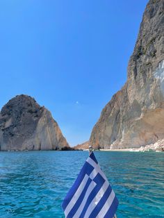 the greek flag is waving in front of some mountains and water with rocks on either side