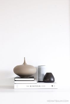 two vases sitting on top of books next to each other in front of a white wall