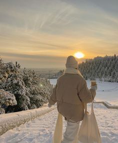 a person walking in the snow carrying two bags and a coffee cup to go with them