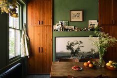 a dining room with green walls and wooden cabinets, fruit on the table in front of an open window