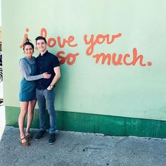 two people standing in front of a wall that says i love you so much